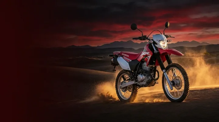 Moto trail rouge soulevant le sable sur une dune du désert, au coucher du soleil